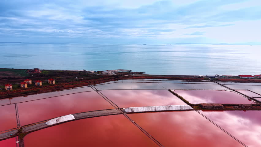 Flight over the pink salt farms at sunset. Blue endless waterscape and overcast sky at backdrop.