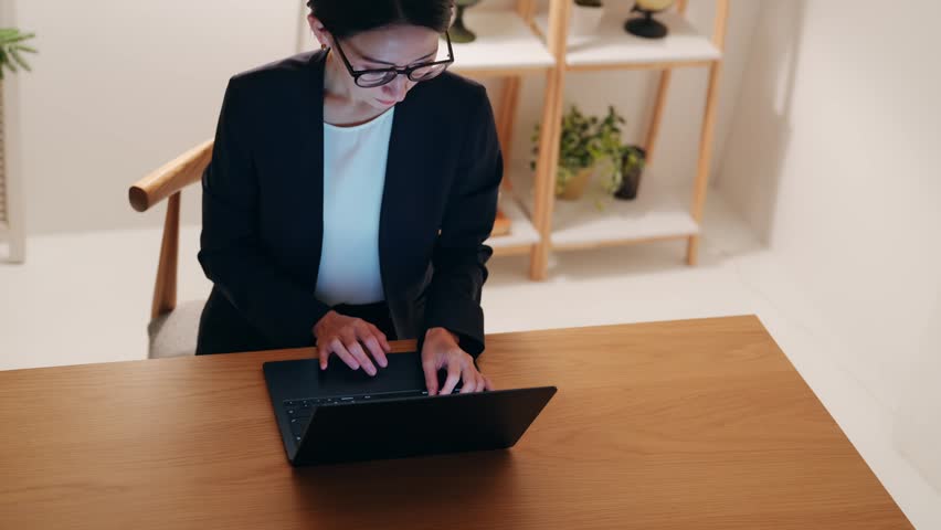 A middle-aged woman looking at a computer in a dark room. Desk work, remote work, freelance, work, systems engineer, engineer.