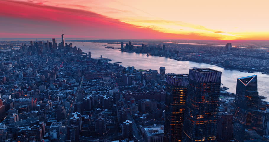 Bright pink and orange sky over the vast panorama of New York, USA. Going down over the urban landscape at the river waterfront at dusk time.