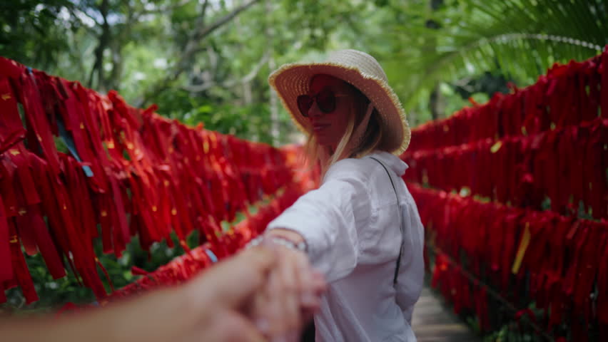 Follow me and travel, happy blonde lady holding hand, trip to Yanoda park, China . Adult woman walking in beautiful rainforest or jungle in summer day, famous tourist attraction, red tapes for wish