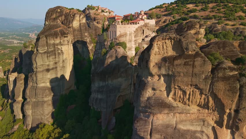 Aerial view of the Varlaam and Great Meteoron monasteries perched on massive sandstone pillars during a misty morning sunrise in Meteora, Greece