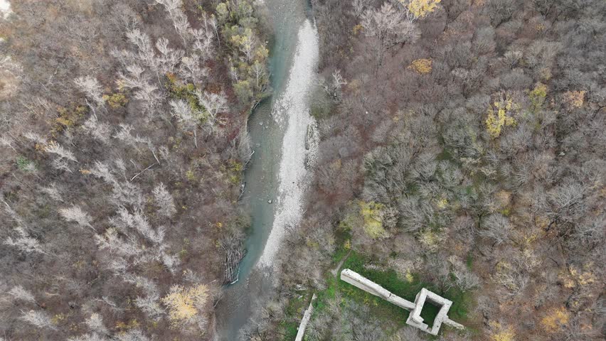 A top-down view of a shallow river bending through forested terrain, revealing ancient stone remains near Ujarma Fortress in soft daylight