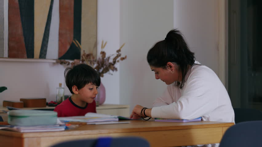Woman leaning beside young boy while he writes with pencil conveying encouragement, calm instruction and nurturing academic guidance in domestic setting