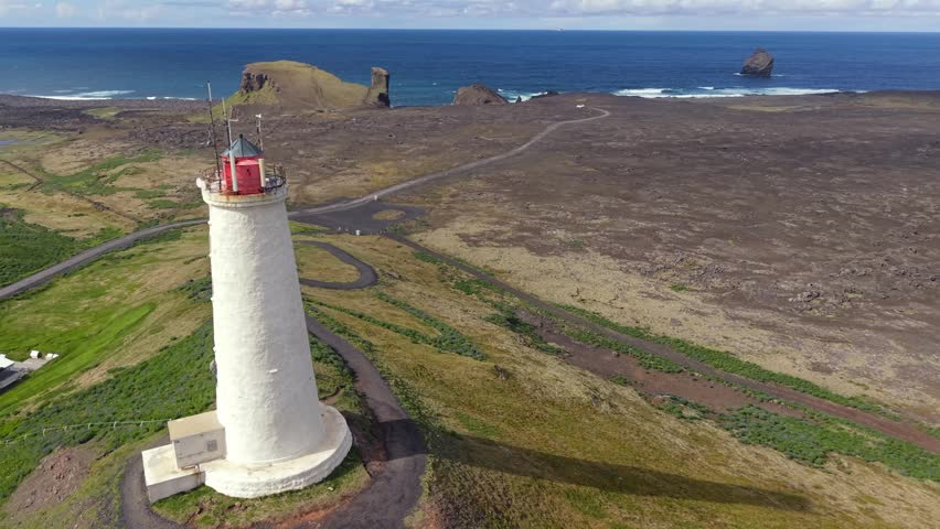 Scenic aerial footage of the historic Reykjanes lighthouse standing on a dramatic cliff overlooking the vast North Atlantic ocean in Iceland