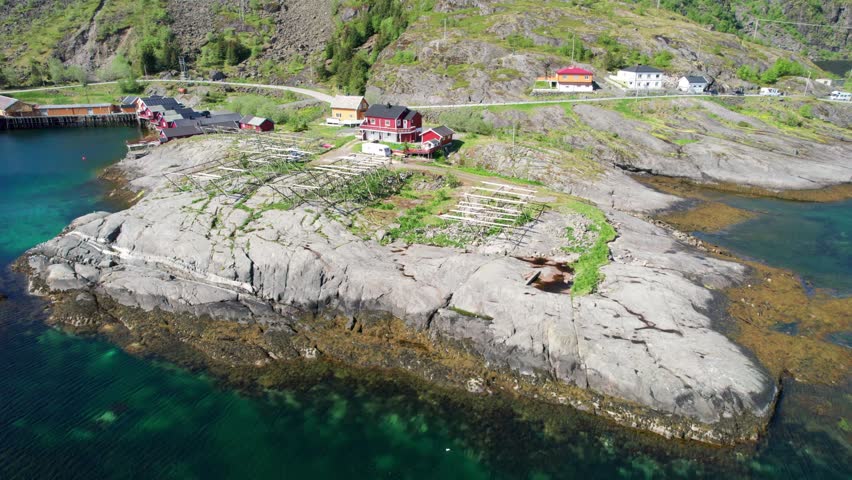 Breathtaking aerial footage flying over a traditional Norwegian fishing village with cod drying racks on a sunny summer day in Lofoten