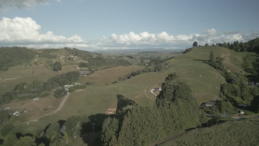 An Aerial view of rolling hills with farmland, scattered trees, and winding rural roads in New Zealand.