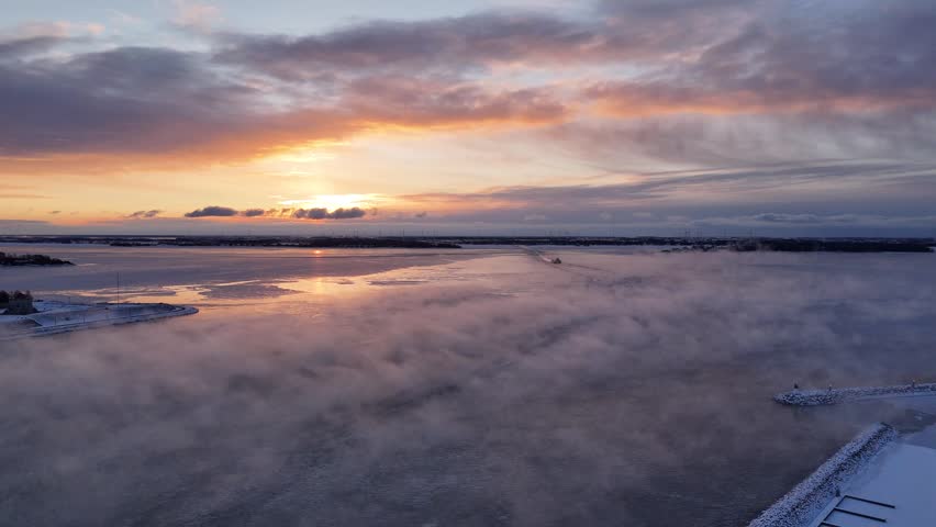 Aerial view of fog drifting over wide frozen lake Ontario at sunrise with soft pastel sky in Kingston, Ontario, Canada