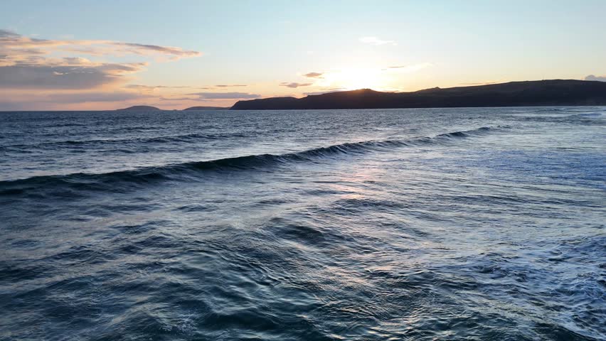 Sunrise over the ocean, waves breaking gently.