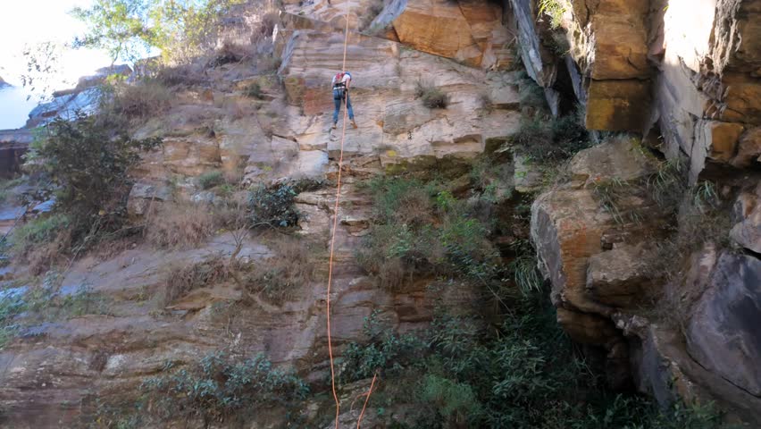 Brave Person Rappelling Down A Steep Rock Cliff Near A Waterfall