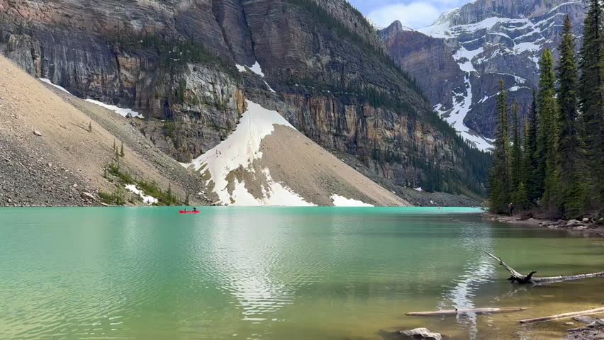Beautiful view on the Moraine Lake in National Park of Banff, Canada. Two kayakers navigate a turquoise lake, framed by towering mountains and snow-capped peaks, with trees lining the shore.