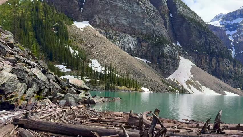 Beautiful view on the Moraine Lake in National Park of Banff, Canada. Beautiful lake surrounded by towering mountains and scattered logs along the shore, showcasing a serene natural landscape.