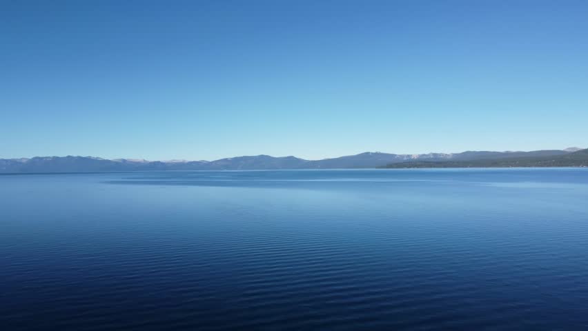 North Lake Tahoe: Lateral aerial shot over blue water, mountains in distance near Kings Beach, CA
