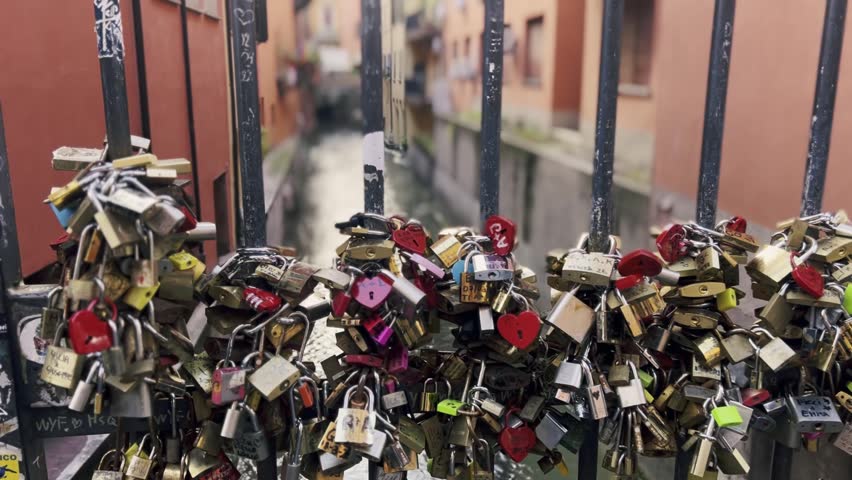 Romantic love padlocks attached to a metal railing on a bridge over a canal in Bologna, Italy, symbolizing eternal love and commitment with many colorful heart-shaped locks from lovers