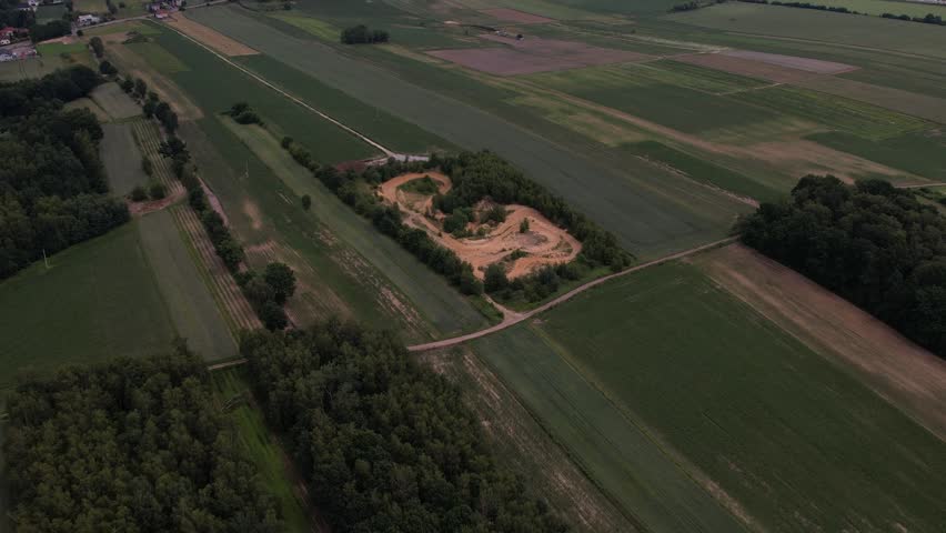 Expansive aerial view of a dirt bike track nestled among green agricultural fields and forests