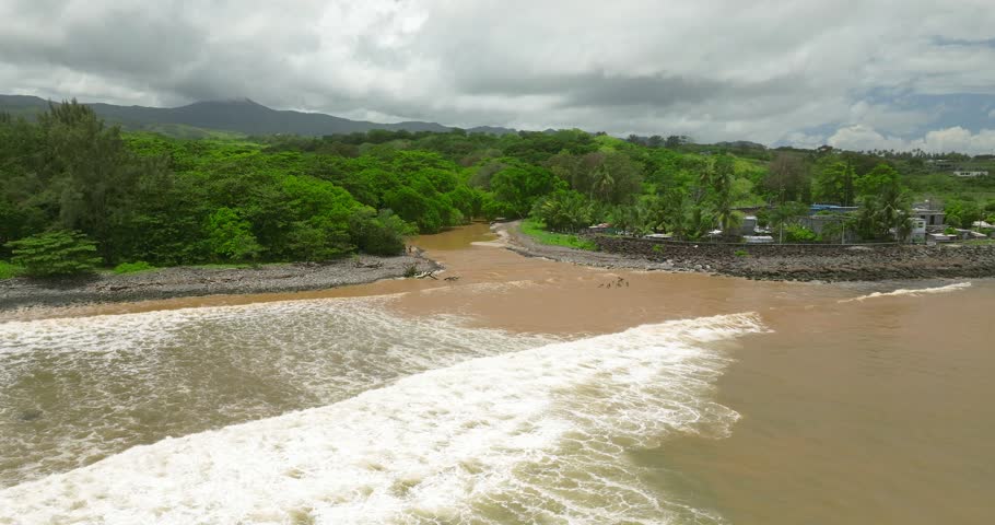 An aerial view of a river discharging sediment-rich water into the ocean, forming visible foam and a halocline along the shore