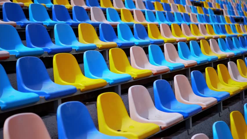 Wide view of empty plastic seating inside a modern sports arena before spectators arrive. Bright colors and orderly rows illustrate preparation for competitions, concerts, and large public gatherings.