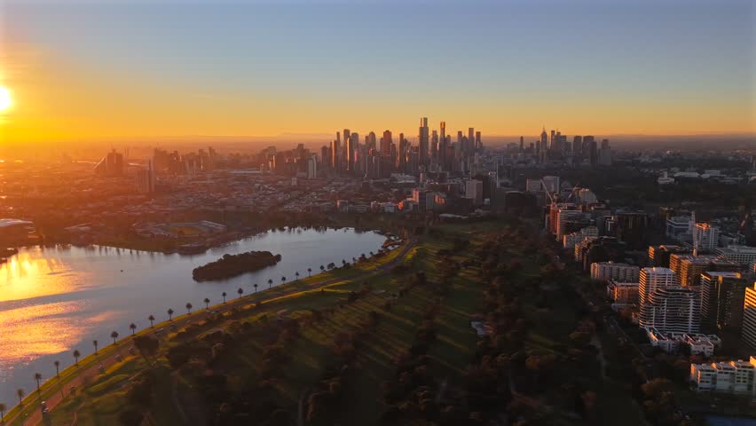 Aerial drone video flying left at sunset over Albert Park, revealing more of Albert Park Lake, the golf course, South Melbourne, Southbank and Melbourne CBD