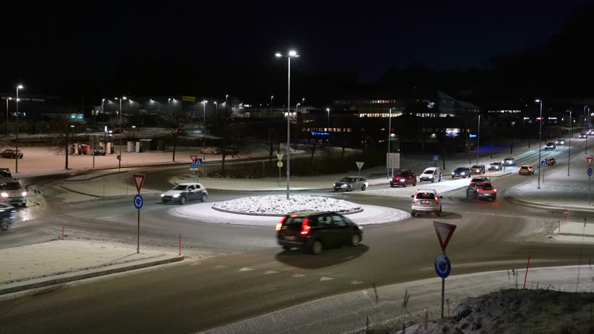 A wide-angle shot of early morning traffic passing through a snow-covered roundabout in the Lokkemyra commercial district in Kristiansund, Norway