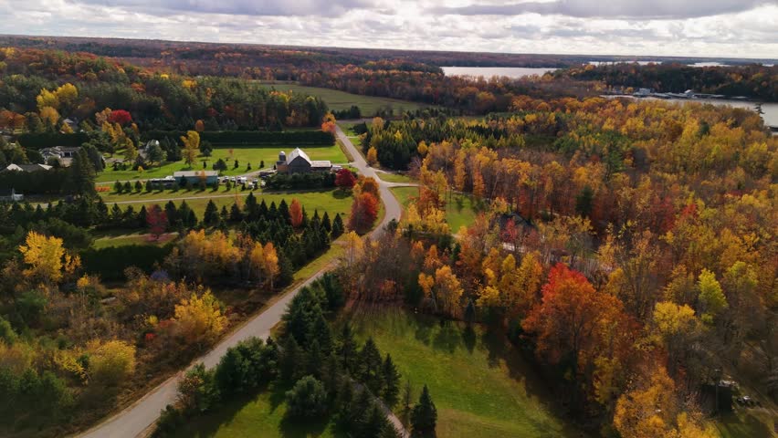 A drone view of waterfront farmland and a winding country road in the Muskoka region near Bracebridge, Ontario, Canada, surrounded by autumn forest