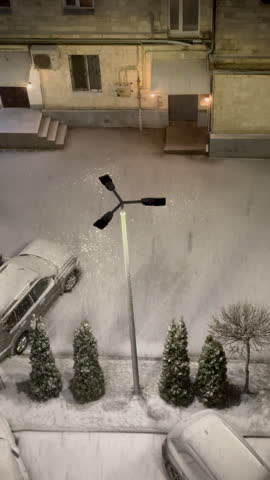 Snow falling at night in courtyard with street lamp, vertical background