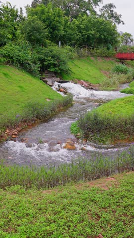 Open green spaces surround a meandering stream, which passes over rocky tumbles and flows through manicured gardens.
