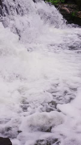 A close-up view of the white foam and surging water after the waterfall hits the rocks gives a strong sense of water flow.