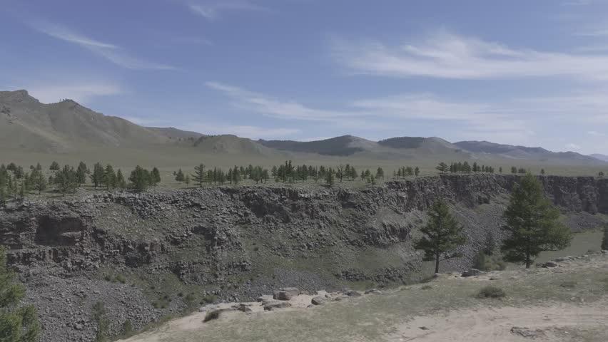 An aerial view of a rocky canyon rim lined with scattered trees and forested slopes at Tsetserleg-Tariat Canyon in Mongolia under bright daylight