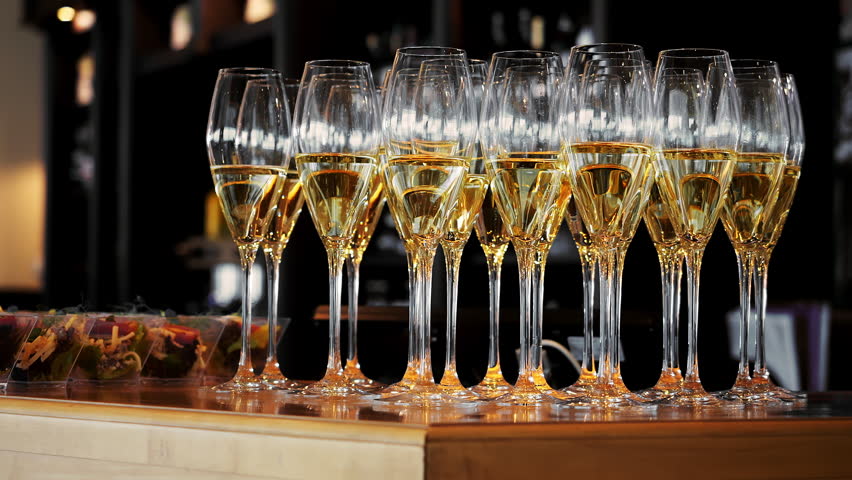 Rows of champagne glasses filled with sparkling wine on a bar counter before a reception or celebration. Elegant catering setup for weddings, parties and corporate events.