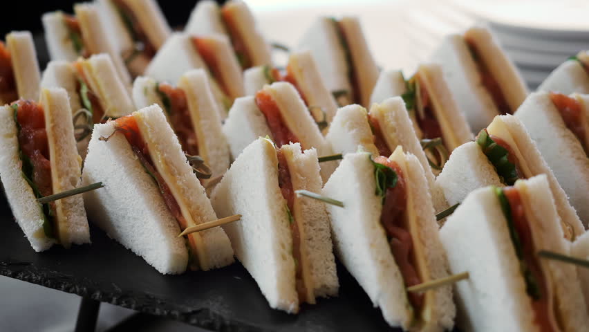 Fresh mini sandwiches with smoked salmon, cheese and greens served on a catering buffet. Elegant finger food for wedding reception, corporate event, party or hospitality service.