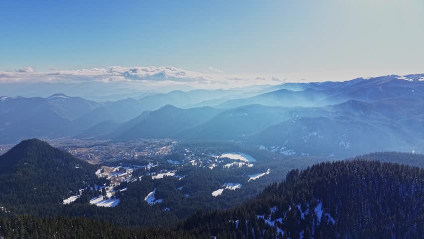 The Carpathians mountains in Bulgaria, covered in snow. The sun shines over the hills. The town and valleys lie below, creating a vast landscape in winter.