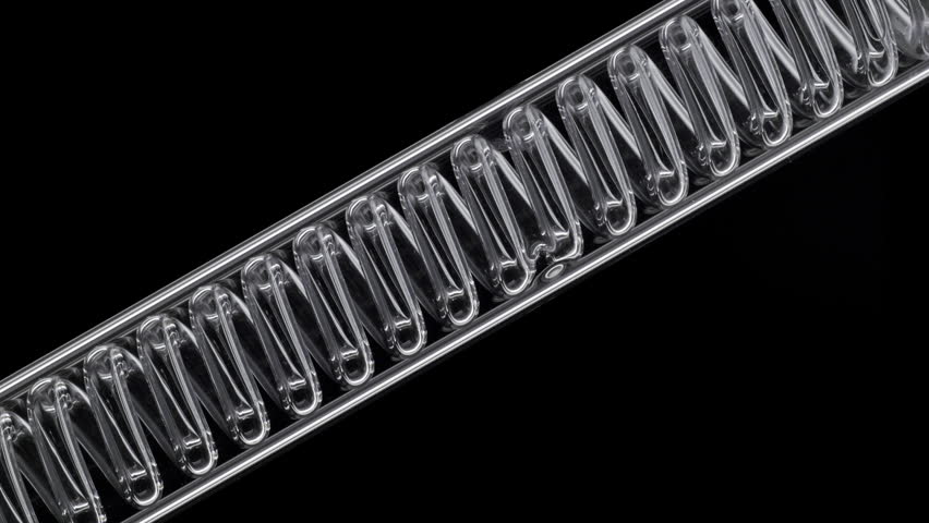 Full-frame close-up of luminous violet fluid flowing through an inclined coil laboratory condenser, filling it up on pitch-black backdrop | Butterfly pea flower tincture cosmetic element concept
