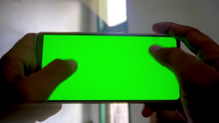 A person holding and playing on a smartphone with a green screen display, capturing mobile gaming, application use, and digital technology concepts in a horizontal view.