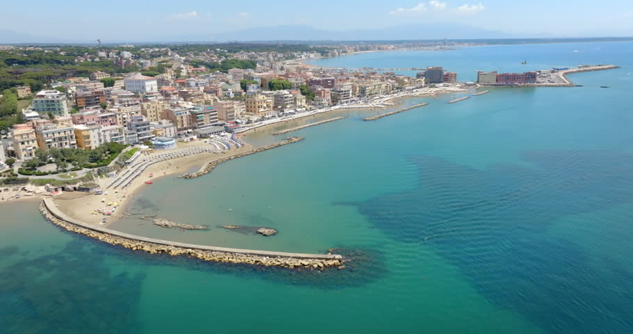 Aerial view of Anzio, near Rome, Italy, showing the historic port, breakwaters protecting the harbor, sandy beaches with sun umbrellas, and the city