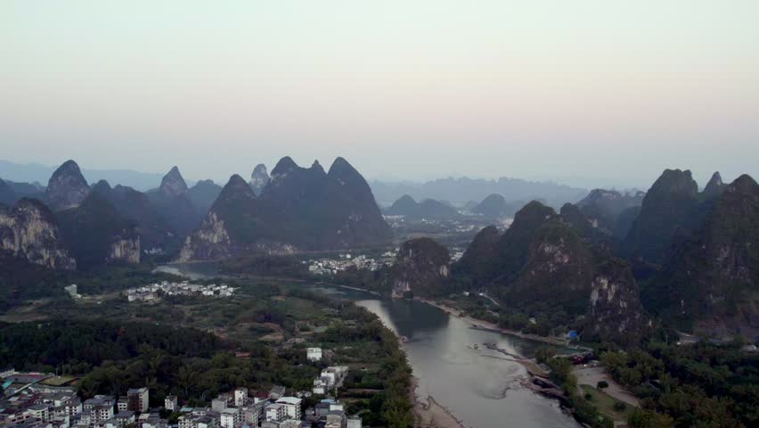 Aerial view of distinctive karst peaks, a winding river, and small settlements in a rural natural landscape under pale sky.