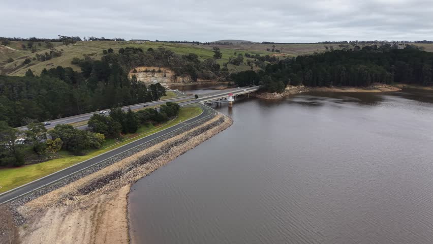 Aerial view of a large reservoir, dam wall, and a bridge with traffic on an overcast day near melbourne