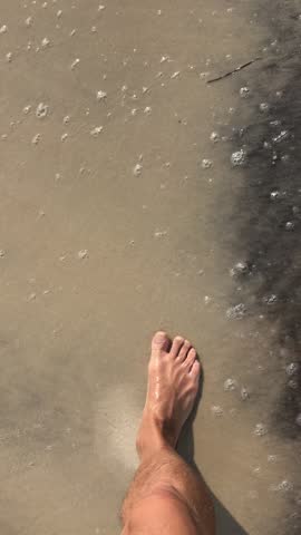 POV footage of barefoot walking along a sandy beach at the water