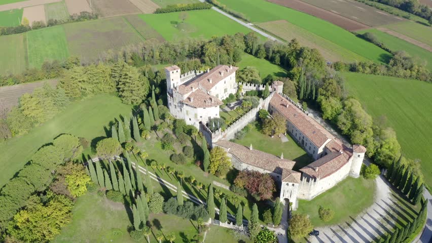 An aerial view of Castello di Villalta in Udine, Italy, encircled by vineyards and green fields under bright daylight