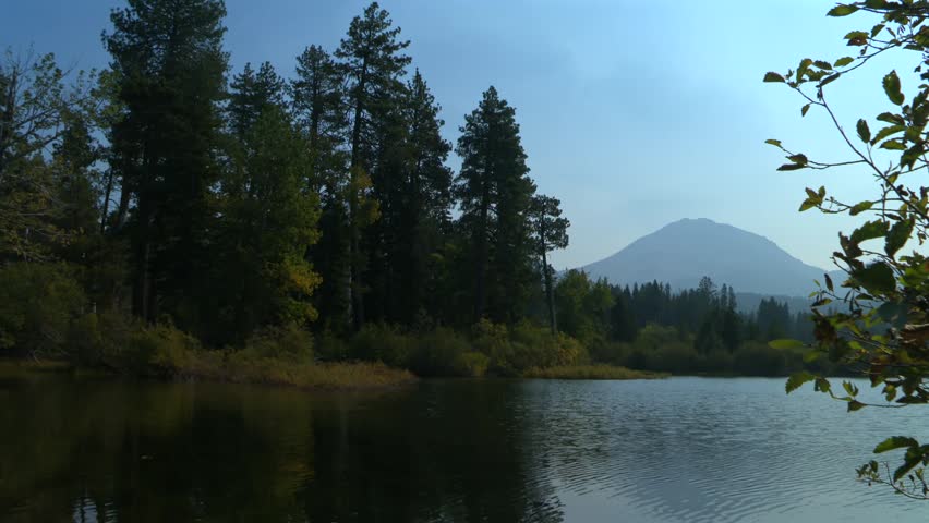 Manzanita Lake surrounded by tall conifer trees with mountain rising in the background at Lassen Volcanic National Park, California, USA. Static shot