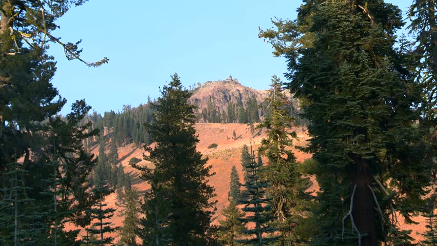 Rocky mountain ridge surrounded by tall conifer trees and forested slopes in Lassen Volcanic National Park, California, USA. Static shot