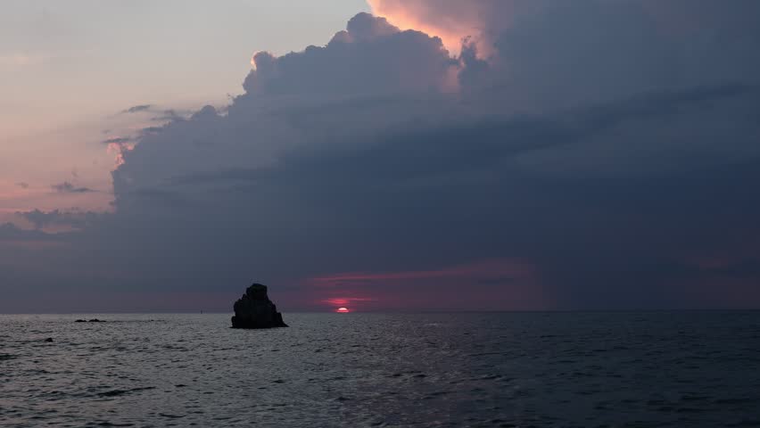 Fiery crimson sunset behind a lone rock silhouette over the calm Tyrrhenian Sea, Spiaggia Michelino, Tropea, Calabria, Italy