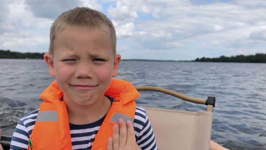 A cheerful child in a bright orange life jacket enjoys a safe boat ride on calm waters, showcasing the importance of water safety gear while capturing the joy and freedom of a sunny day out on lake