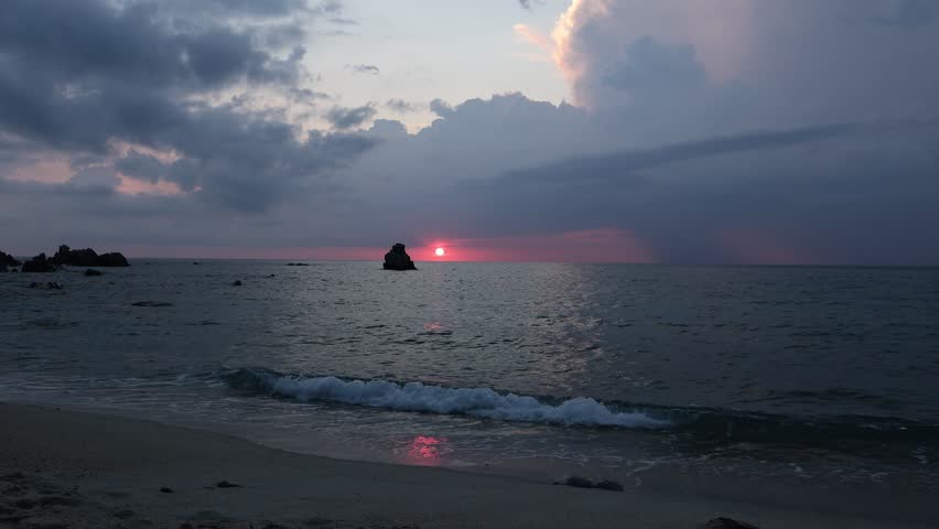Fiery crimson sunset behind a lone rock silhouette over the calm Tyrrhenian Sea, Spiaggia Michelino, Tropea, Calabria, Italy