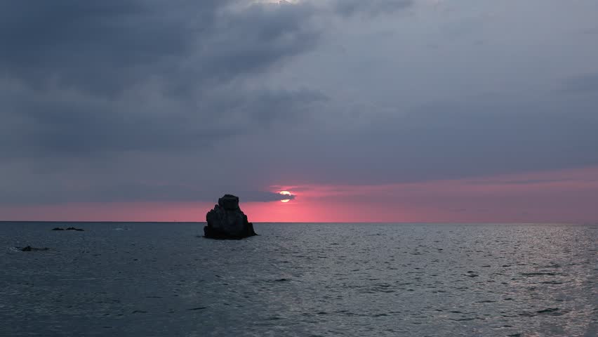 Fiery crimson sunset behind a lone rock silhouette over the calm Tyrrhenian Sea, Spiaggia Michelino, Tropea, Calabria, Italy