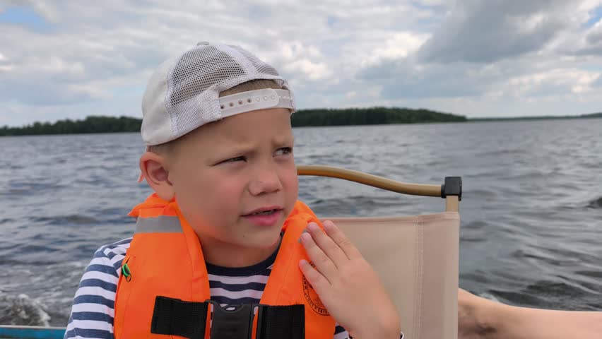 A cheerful child in a bright orange life jacket enjoys a safe boat ride on calm waters, showcasing the importance of water safety gear while capturing the joy and freedom of a sunny day out on lake
