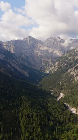 Vertical aerial view of a dramatic alpine valley with rugged limestone peaks, dense evergreen forest and winding mountain river near Eng Alm in Tyrol, Austria