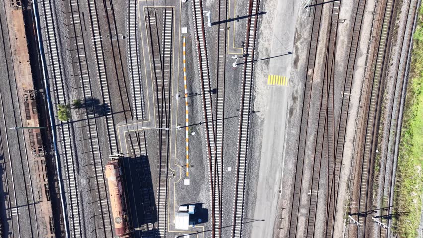 Railway station with multiple tracks and a freight train passing through in a sunny day from above