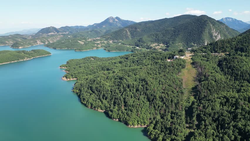Drone flyover above emerald water and pine covered hills at Lake Plastiras in Karditsa region Greece for Mediterranean alpine ecosystem and travel destination concept. High quality 4k footage