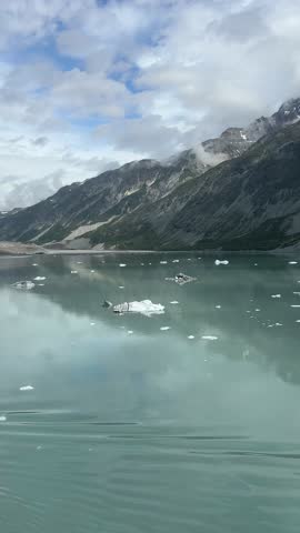 Peaceful Alaska lake with floating icebergs and mountain reflection under cloudy sky