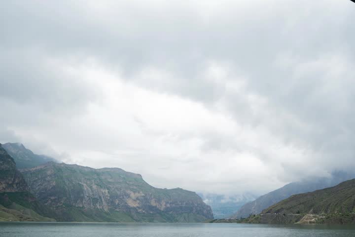 Rain clouds fill the sky over a large mountain lake that is bordered by tall mountains. 