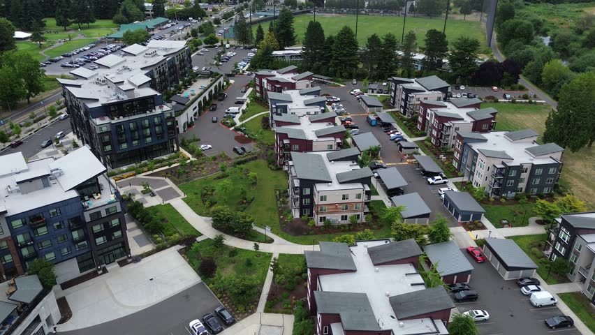 Pedestrian walkways intersect landscaped lawns surrounding contemporary apartment buildings. Dense tree canopies frame the multi family residential neighborhood in Kent, King County, WA. USA